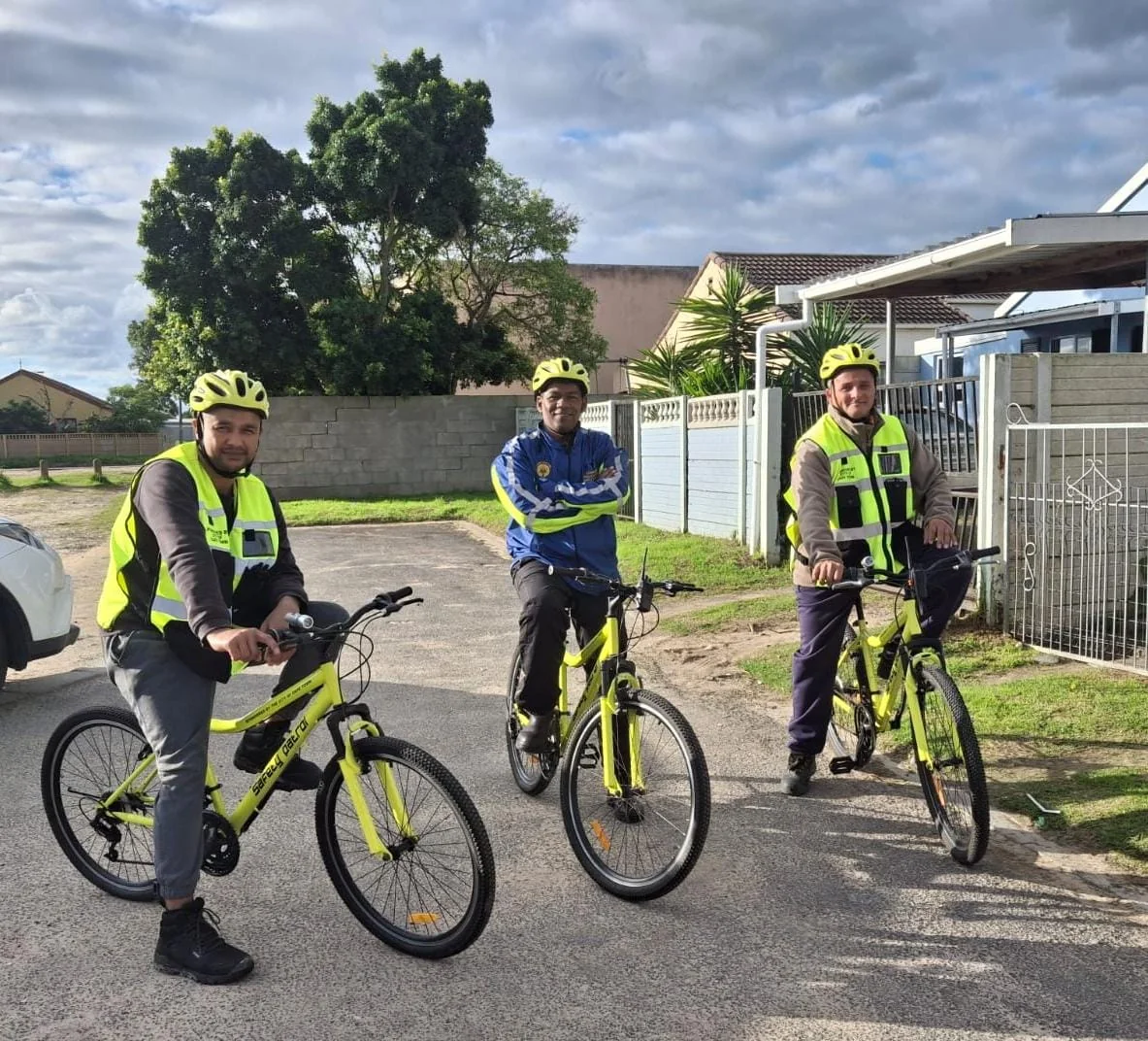 Three neighbourhood-watch participants with high-visibility bicycles on a residential street.